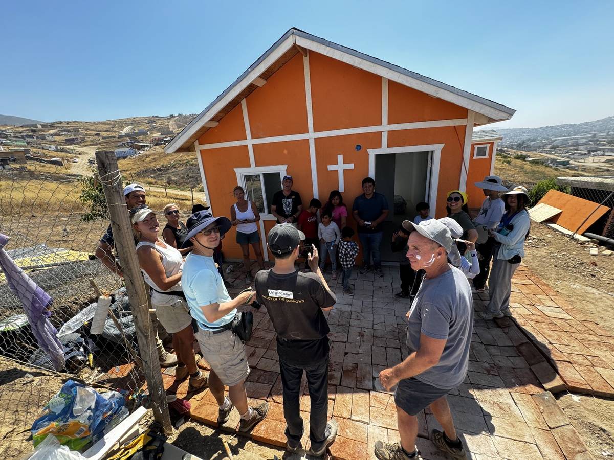 Volunteers and family at a finished orange home with a cross