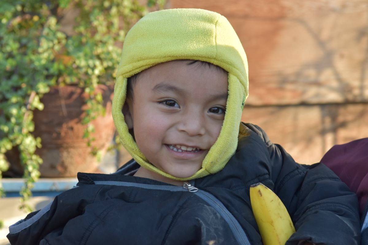 A toddler in a yellow hood holding a banana