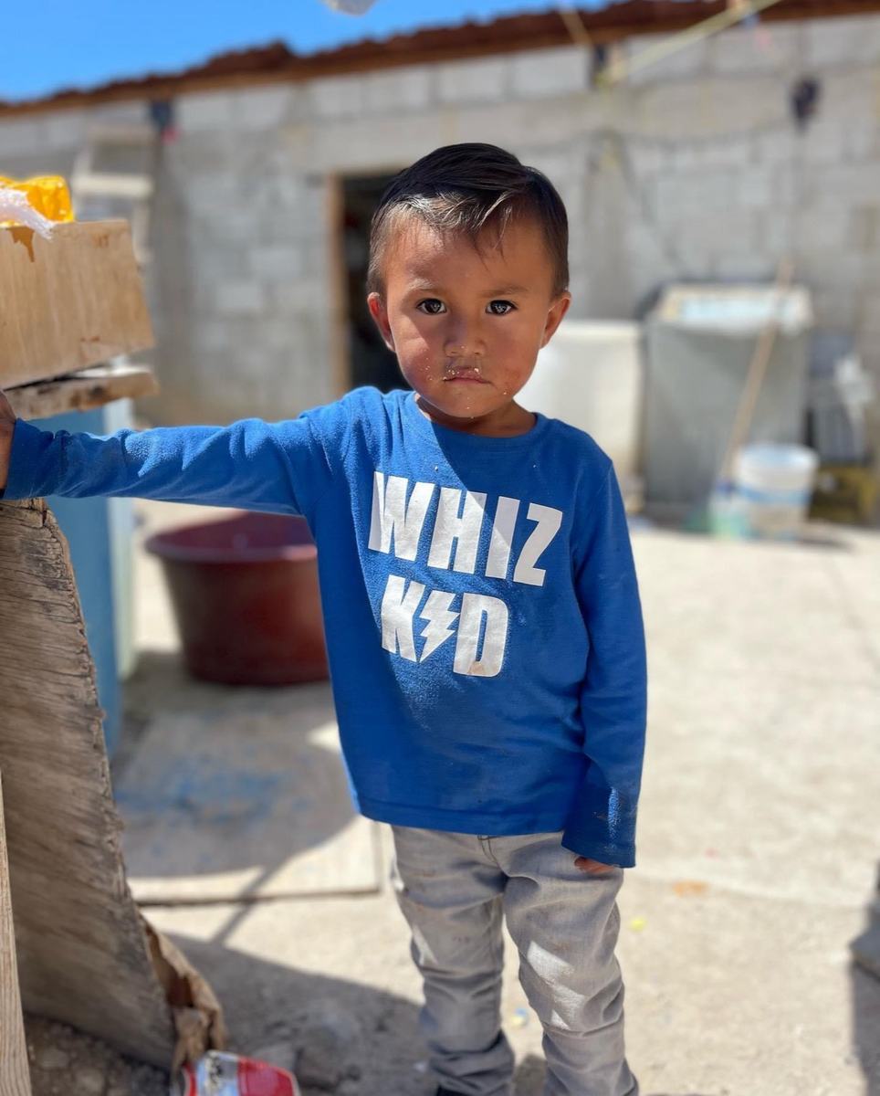 A little boy in a blue Whiz Kid shirt outside his home