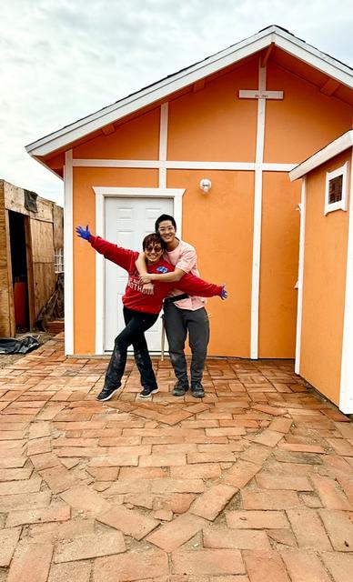 Two volunteers celebrating in front of an orange home