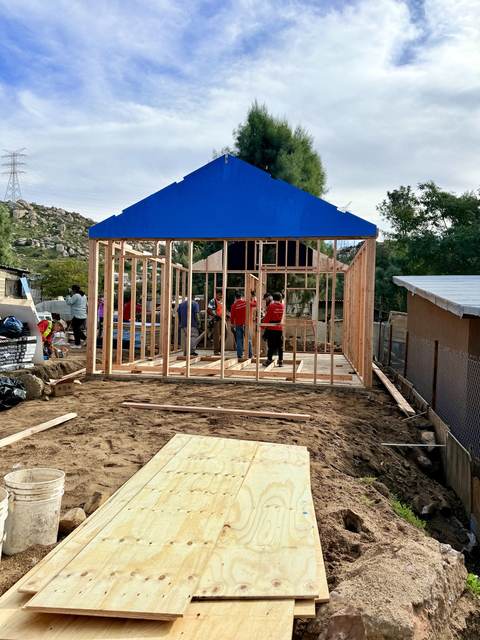 A framed home under a blue tarp roof