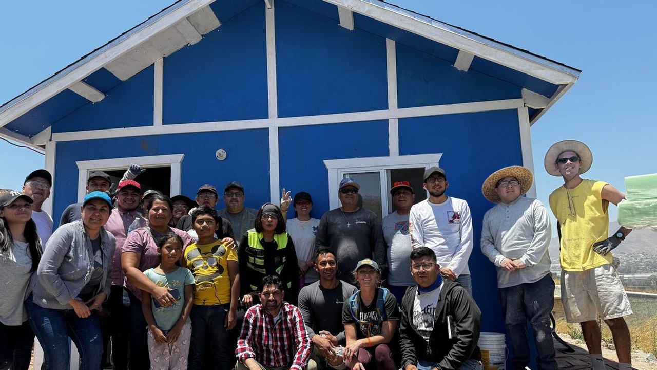 Club Dust volunteers and a Tecate family in front of a finished blue home